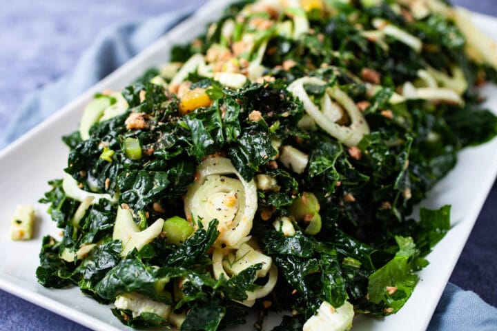 A large serving plate with a raw kale salmon salad.