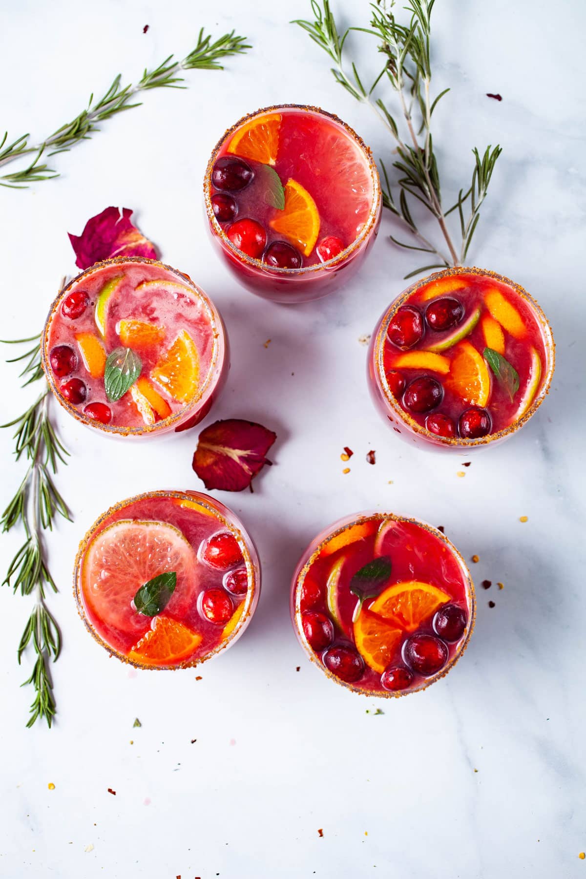 Pomegranate drinks garnished with fresh fruits and mint displayed on a table.