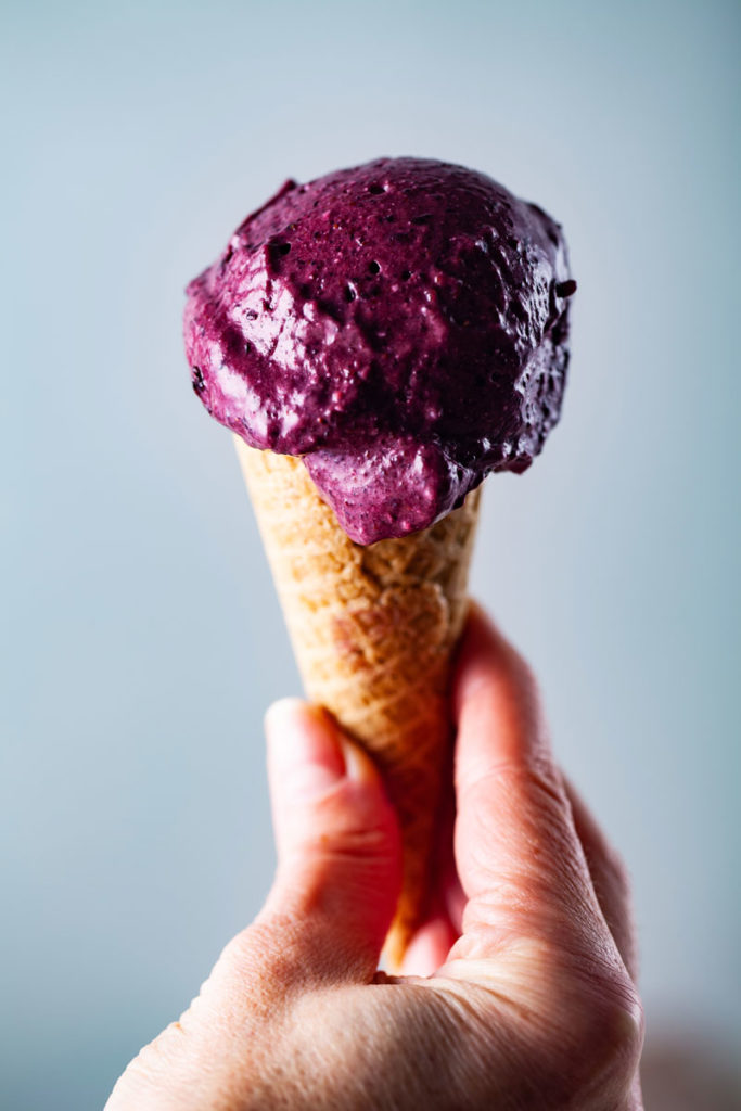 A hand holding a creamy berry ice cream in a cone.