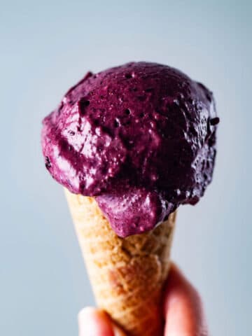 A hand holding a creamy berry nice cream in a cone.