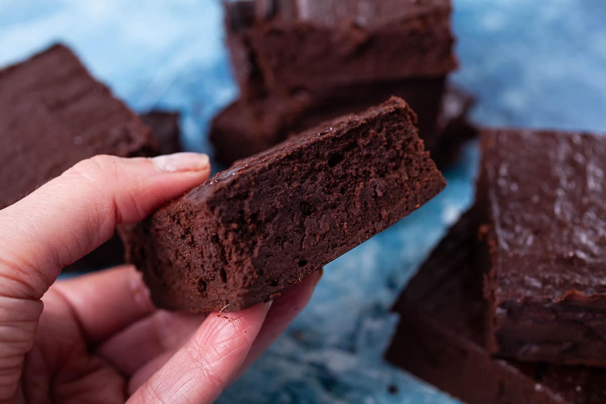 A hand holding a no flour brownie with a shiny crust.