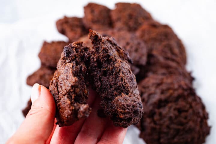 A hand breaking a soft baked flourless peanut butter cookie in half.