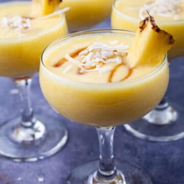 Pina colada mocktail drinks garnished with coconut shreds, a drizzle of maple syrup and fresh pineapple slices.