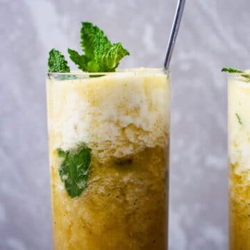 A large spoon in a sparkling pineapple mocktail drink with mint in a tall glass.