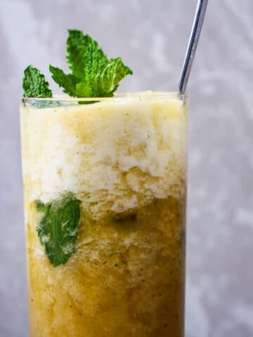 A large spoon in a sparkling pineapple mocktail drink with mint in a tall glass.