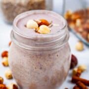 A creamy nut smoothie on a table, garnished with hazelnuts.
