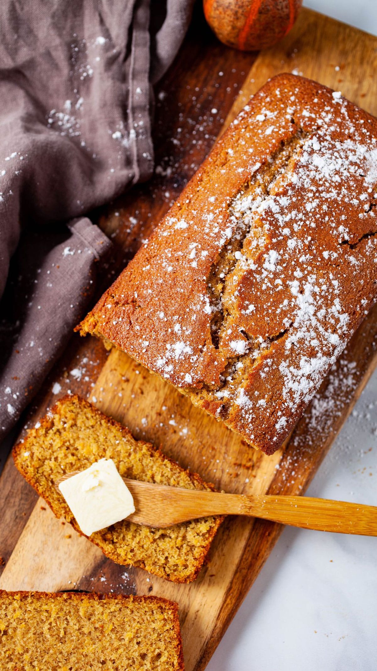A sliced quick bread on a wooden board with butter on knife.