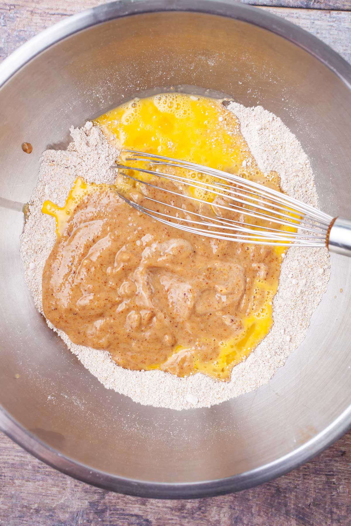 Flour, beaten eggs, and fruit puree in a stainless steel bowl with a whisk.