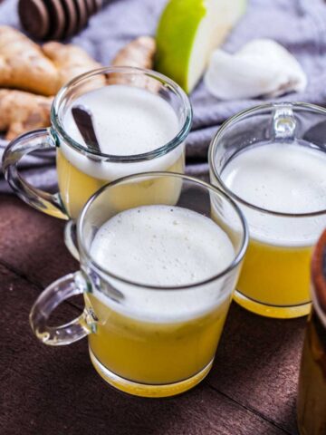 Three small glasses filled with lemon ginger wellness juice.