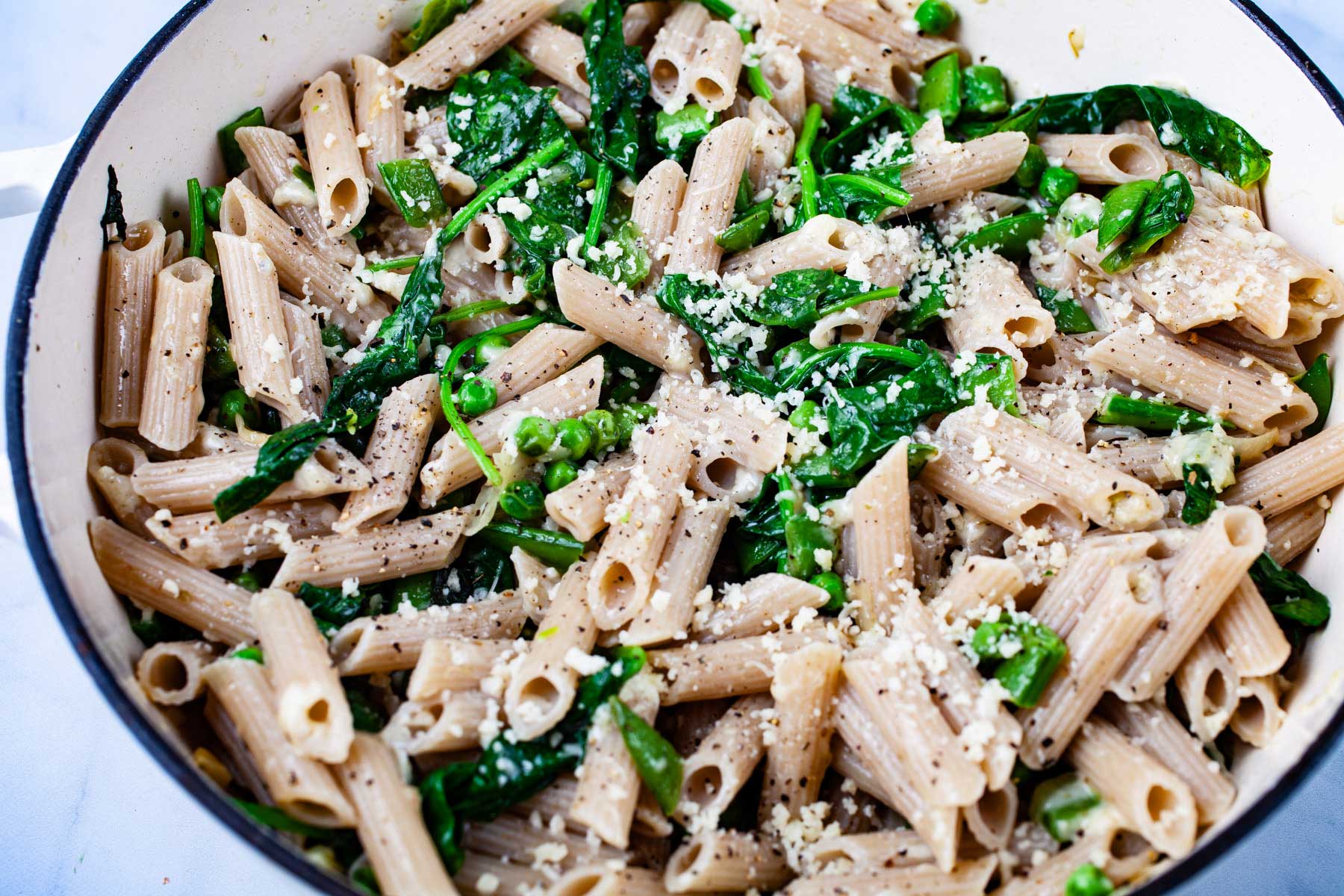 A garlic spinach pasta recipe with peas in a large Dutch pan topped with Parmesan Cheese.