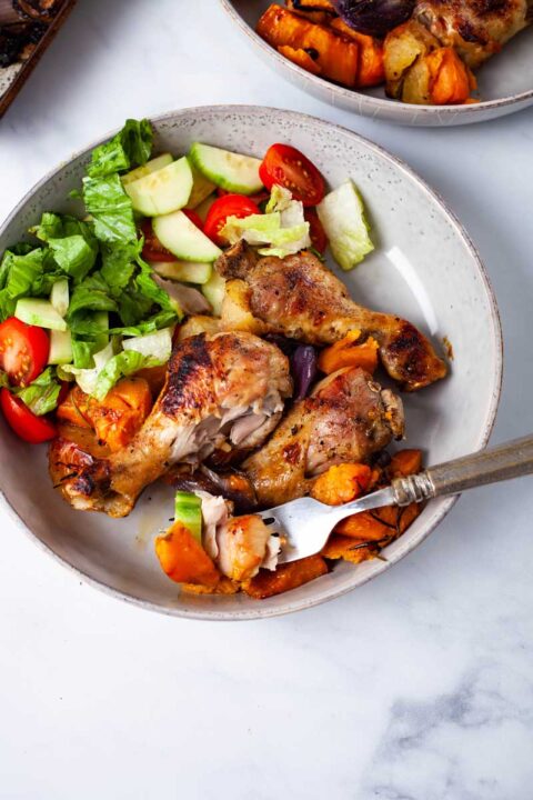 Two plates filled with roasted drumsticks, sweet potatoes and a green salad.