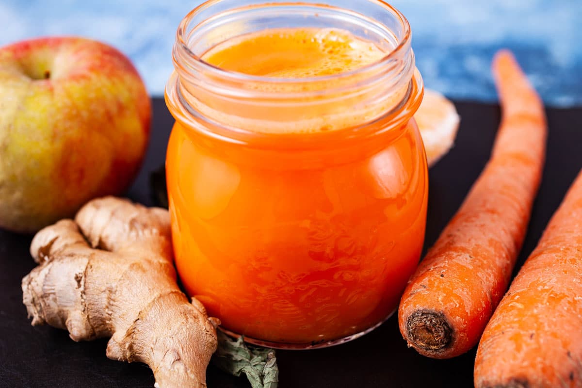 An orange carrot ginger juice in a glass served on a serving board with the ingredients in the background.