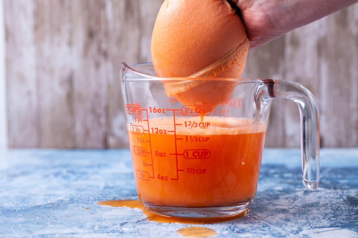 A hand squeezing juice out of a nut milk bag over a measuring cup.