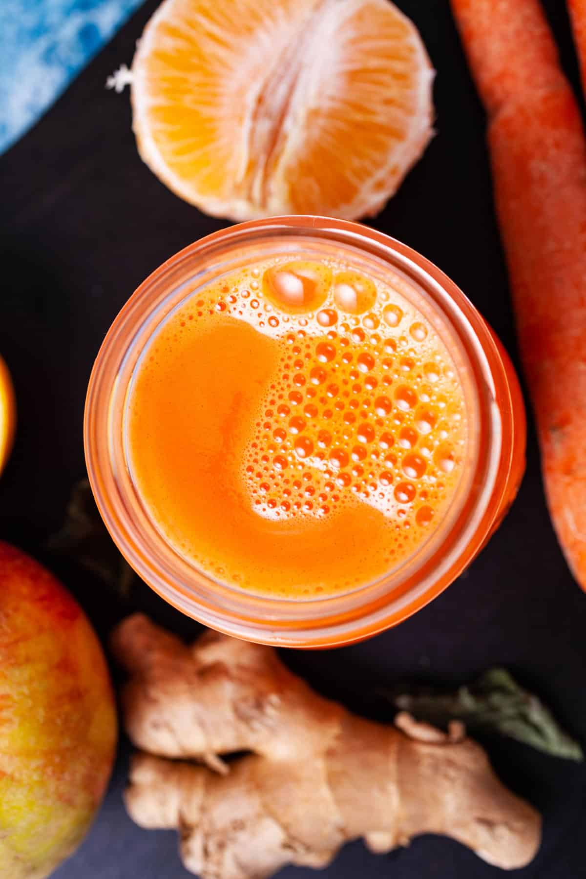 An orange carrot ginger juice in a glass served on a serving board with the ingredients in the background.