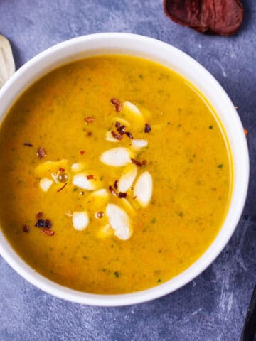 Orange soup in a white bowl topped with shaved almonds and chili flakes.