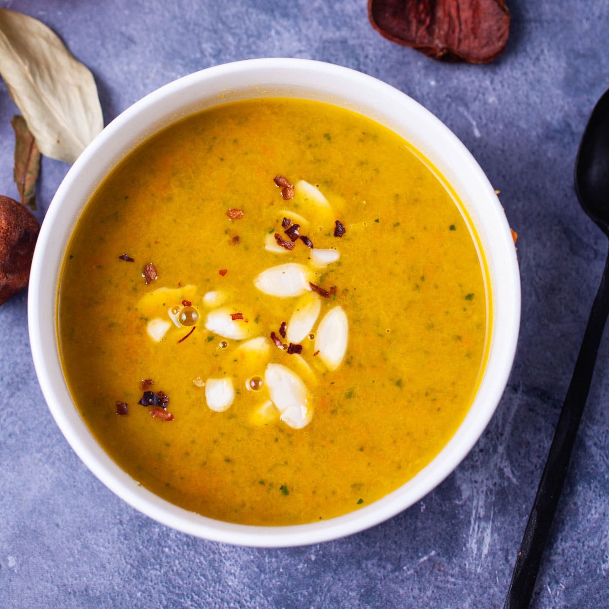 Orange soup in a white bowl topped with shaved almonds and chili flakes.