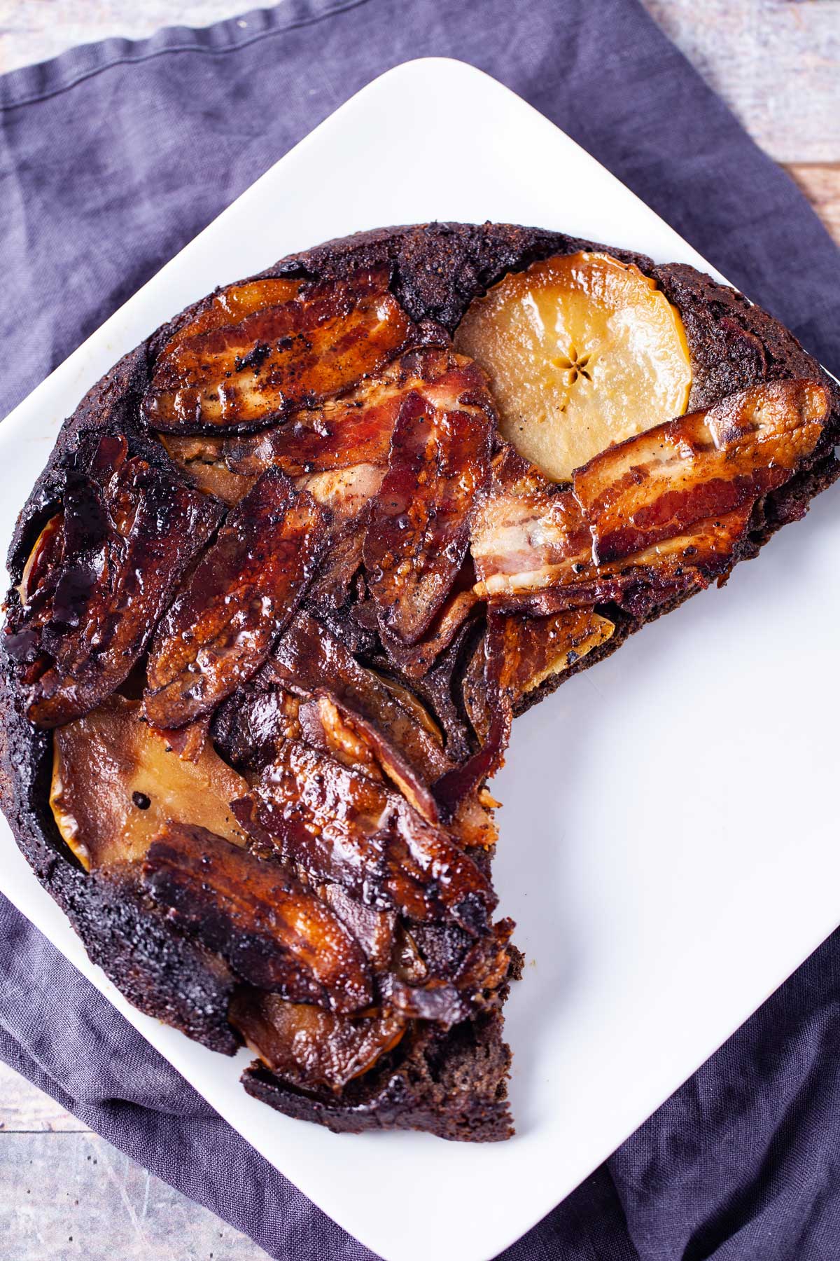 Three fourth of a large apple bacon pancake served on a white square plate.