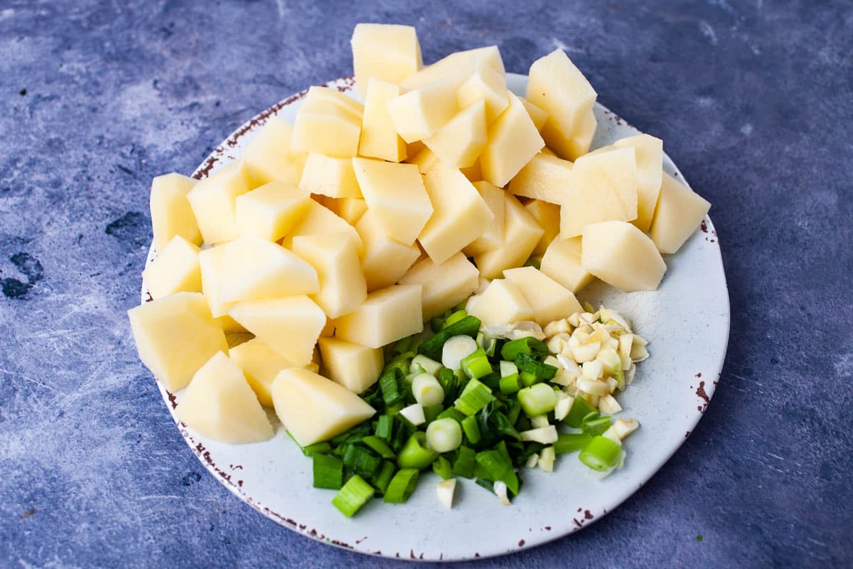 Chopped raw potatoes, chopped green onions, and chopped garlic on a plate.