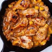 A cast iron skillet with glazed peach chicken legs.