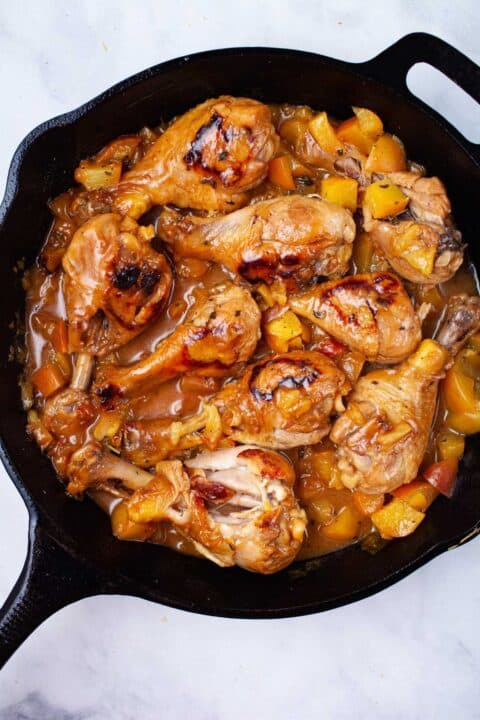 A cast iron skillet with glazed peach chicken legs.