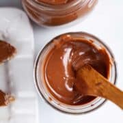 A wooden knife resting in silky, creamy chocolate peanut butter in a jar.