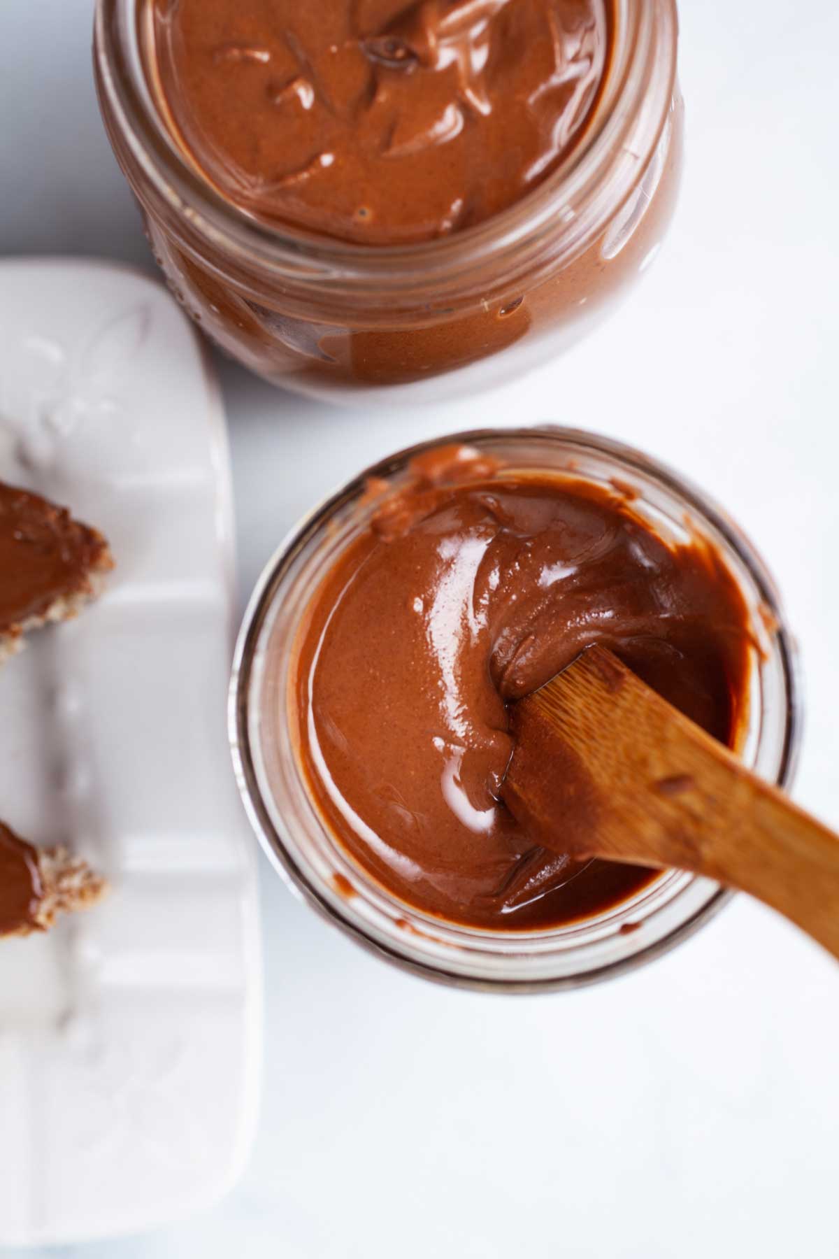 A wooden knife resting in silky, creamy chocolate peanut butter in a jar.