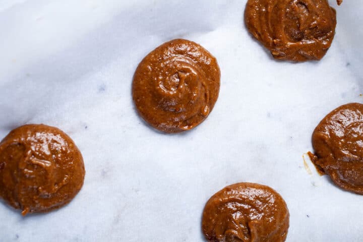 Raw cookie dough drops on parchment paper.