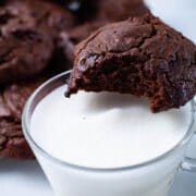 A bitten cookie resting on top of a glass filled with milk.