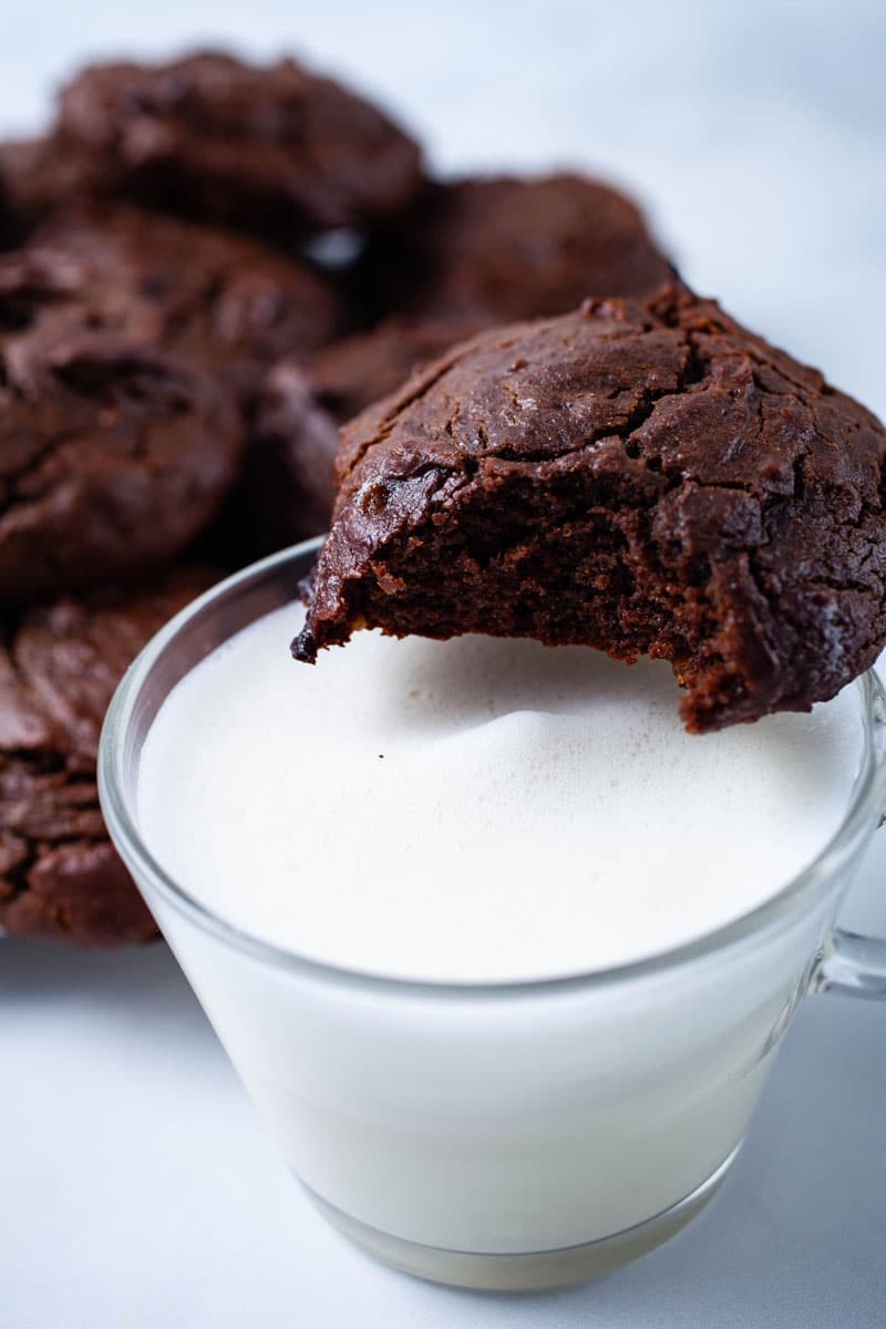 A bitten cookie resting on top of a glass filled with milk.