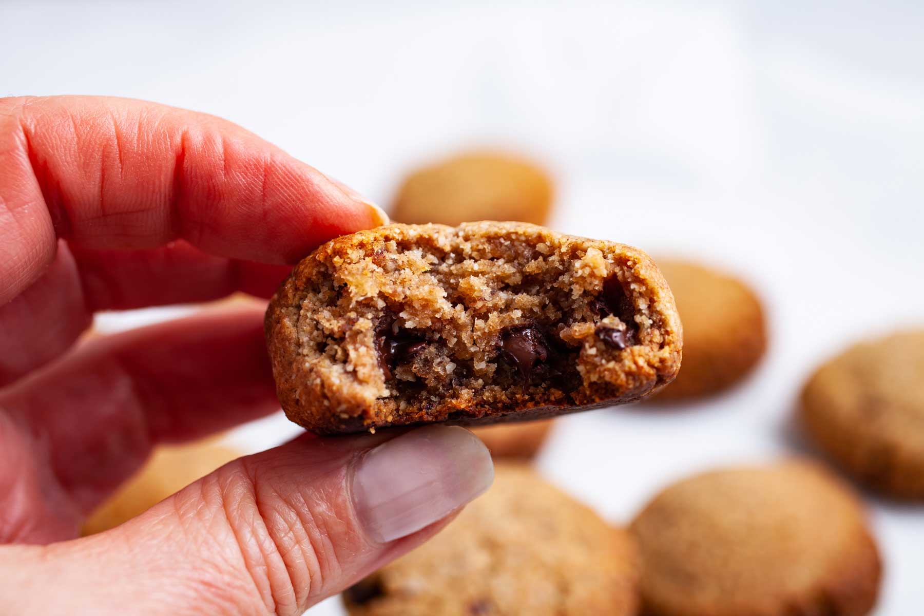 A hand holding a bitten date cookie with chocolate chips.