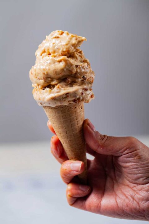 A hand holding a scone topped with two scoops of peanut butter-banana-date nice cream.