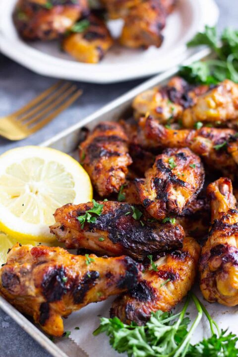 persian grilled wings beside lemon and fresh parsley on a parchment lined baking sheet.