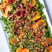 Persimmon arugula salad with a tahini dressing served on a large plate.