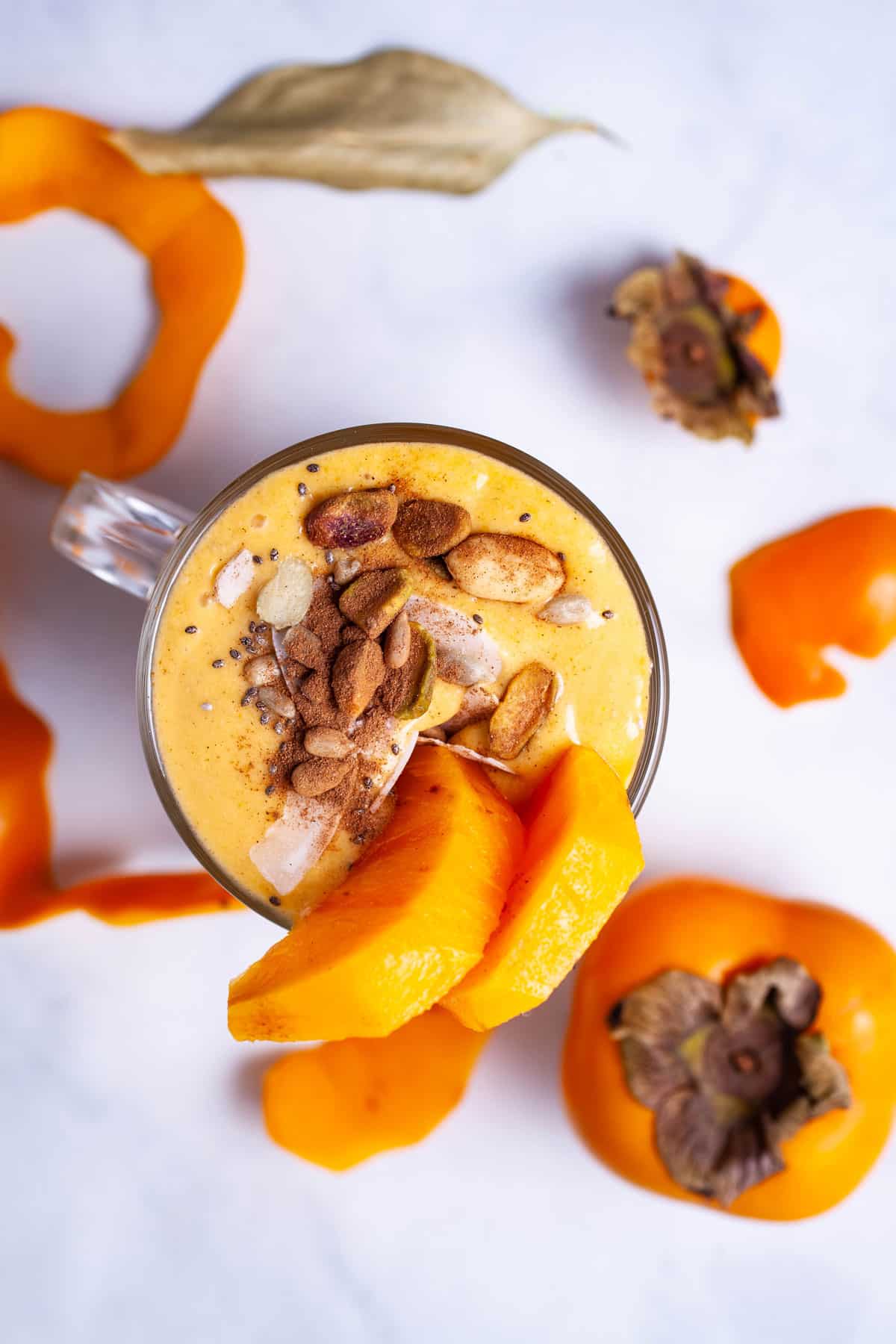 A persimmon smoothie topped with cinnamon, nuts, and garnished with fresh persimmon slices.