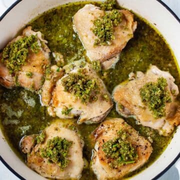 Pan seared chicken thighs with a pesto sauce in a skillet.