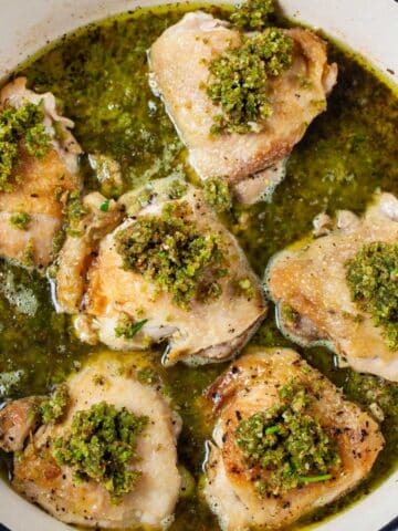 Pan seared chicken thighs with a pesto sauce in a skillet.