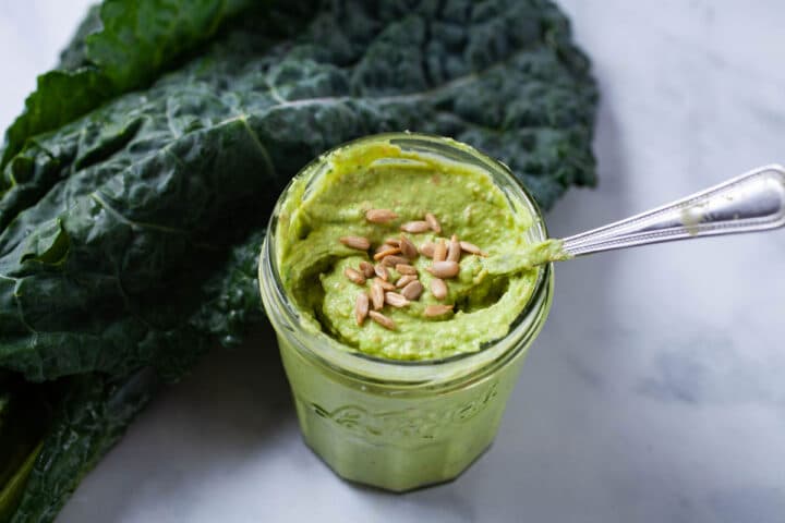 A small spoon resting in a jar filled with a green paste and topped with sunflower seeds.