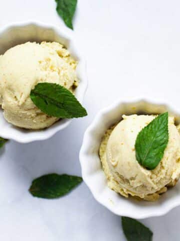 Two small bowls with pineapple avocado ice cream and topped with fresh mint leaves.