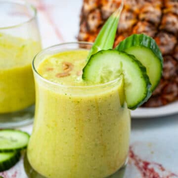 Creamy pineapple cucumber smoothie topped with seeds and garnished with extra cucumber slices.