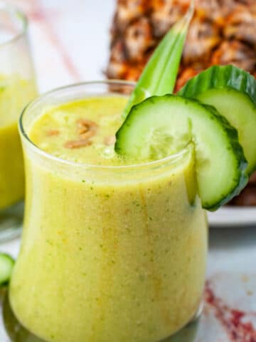 Creamy pineapple cucumber smoothie topped with seeds and garnished with extra cucumber slices.