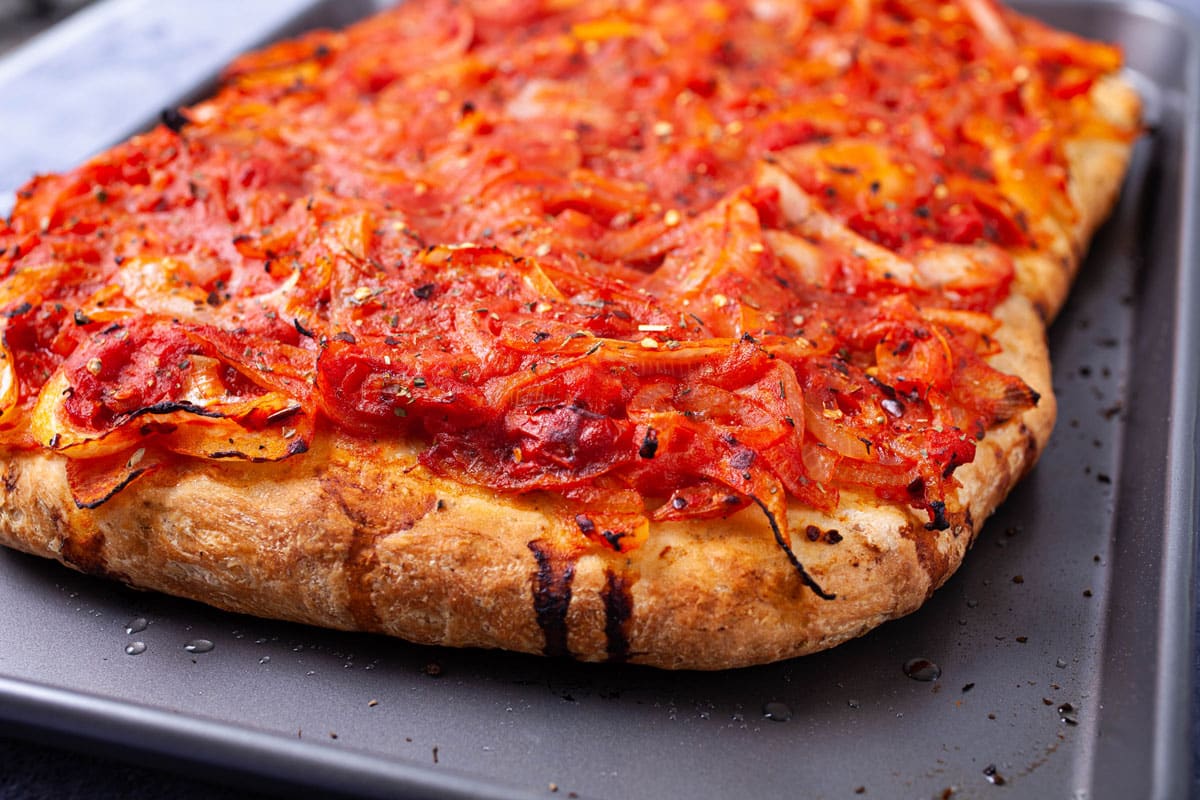 A thick crusted pizza with spicy red sauce onion toppings.