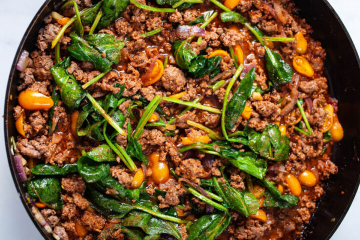 A pan with sauteed ground beef, yellow tomatoes, red onions, and spinach leaves.