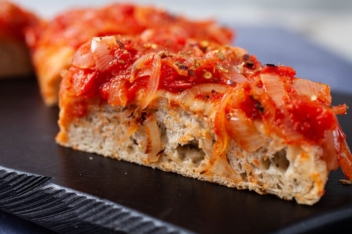 A close up of a squared pepper and onion pizza with a thick crust.