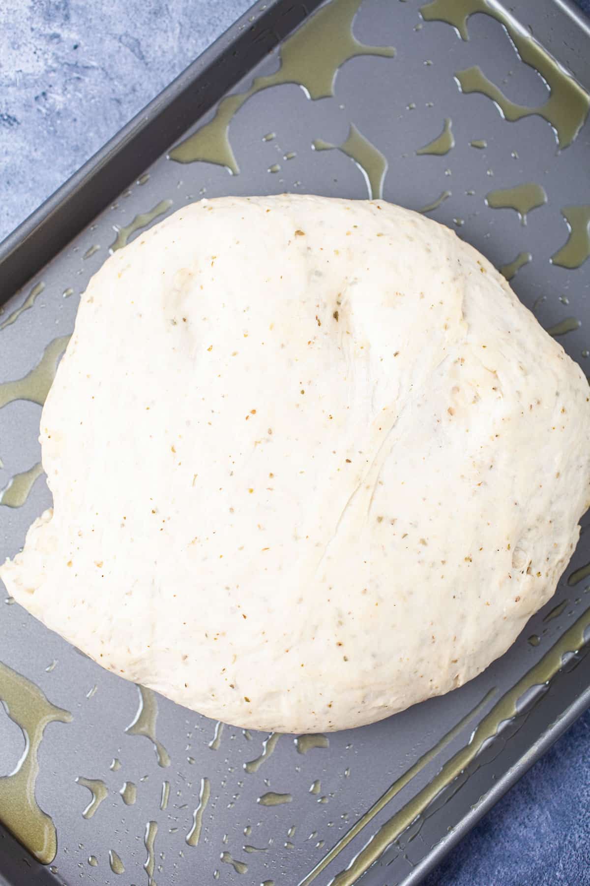 Raw and risen pizza dough ball resting on a large sheet pan.