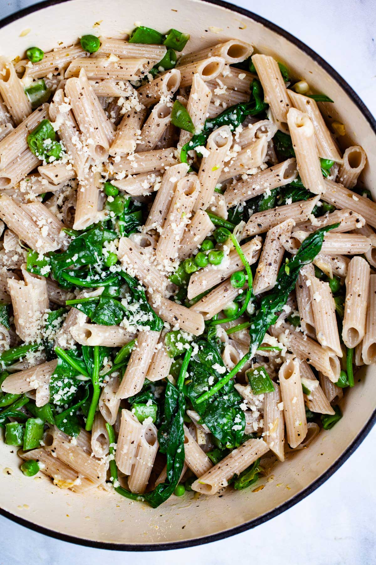 A garlic spinach pasta recipe with peas in a large Dutch pan topped with Parmesan Cheese.