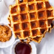 Plantain waffles next to a small bowl with maple syrup and a small bowl with nut butter.