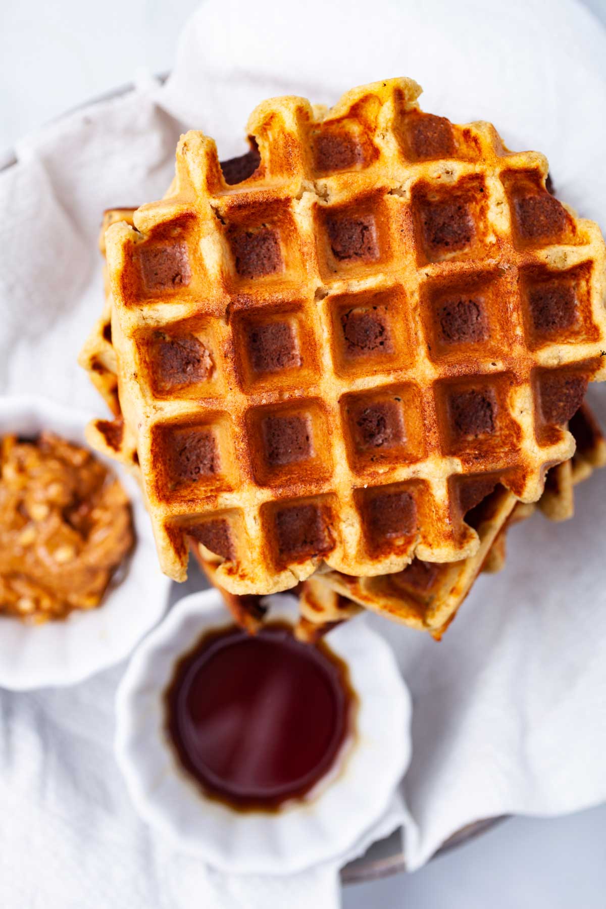 Plantain waffles next to a small bowl with maple syrup and a small bowl with nut butter.