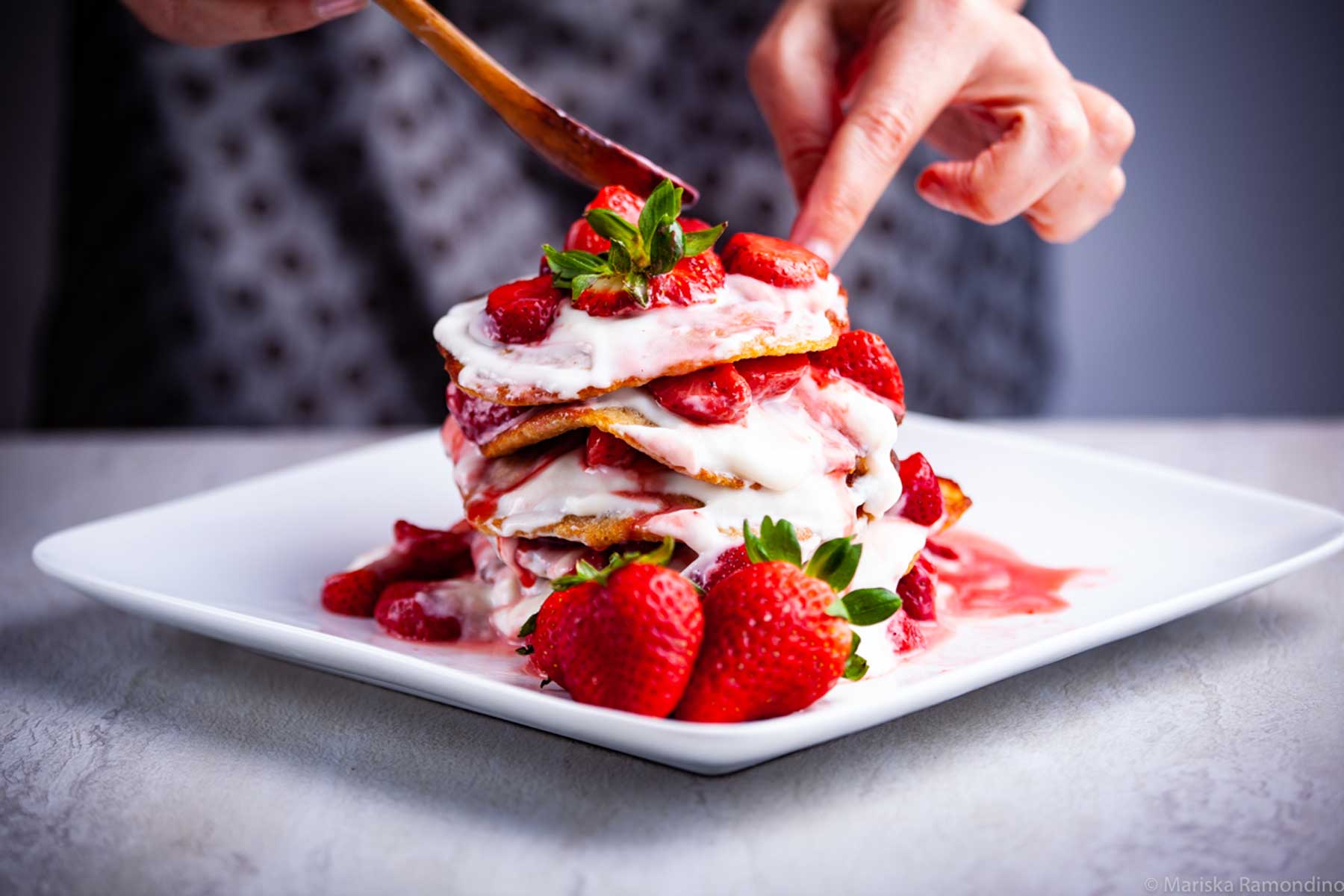 A chef adding extra strawberries on a delicious pancake stack.