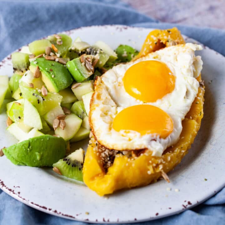 An opened cooked platano filled with eggs and seeds next to a green fruit salad.