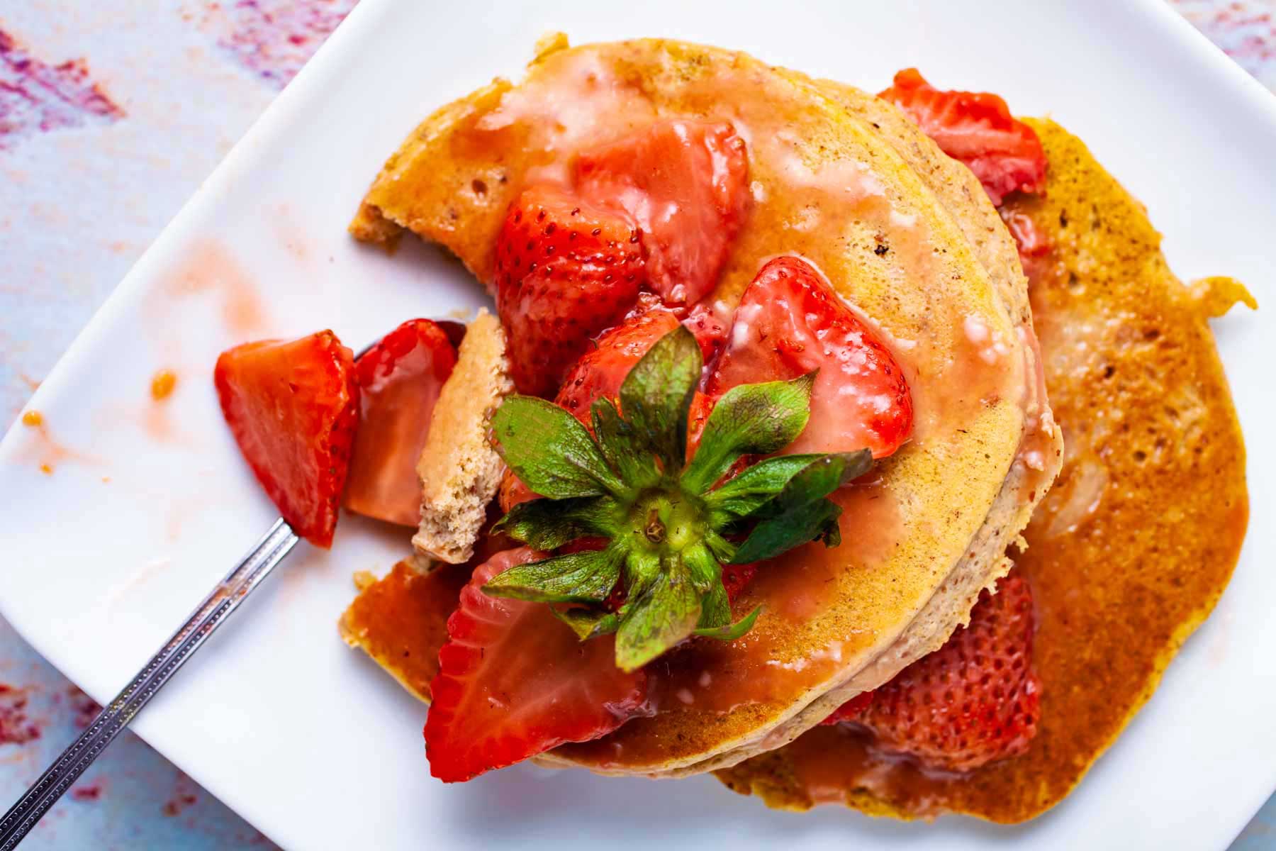 Two plantain pancakes on a plate topped with strawberry sauce.